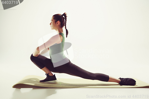 Image of Beautiful slim brunette doing some stretching exercises in a gym