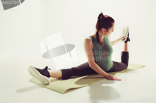 Image of Beautiful slim brunette doing some stretching exercises in a gym