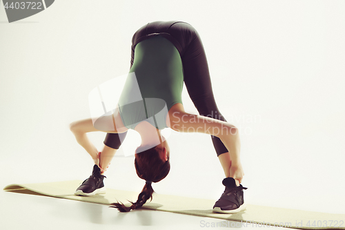 Image of Beautiful slim brunette doing some stretching exercises in a gym