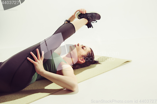 Image of Beautiful slim brunette doing some stretching exercises in a gym