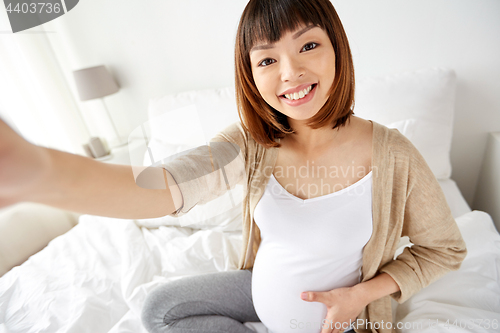 Image of pregnant woman taking selfie in bed at home