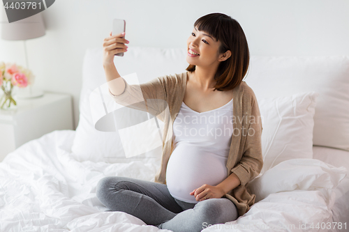 Image of pregnant woman taking selfie by smartphone at home