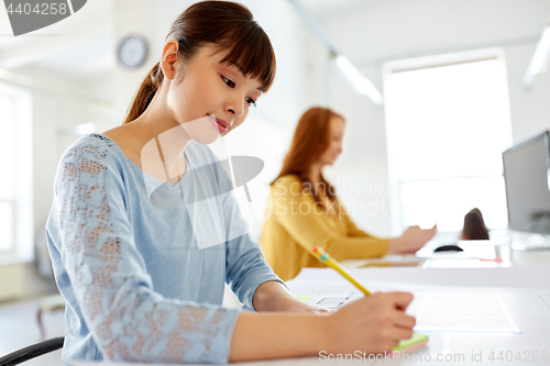 Image of asian woman writing on sticky note at office