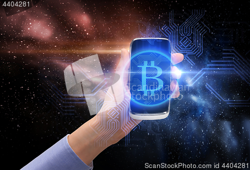 Image of close up of hand with smartphone and bitcoin