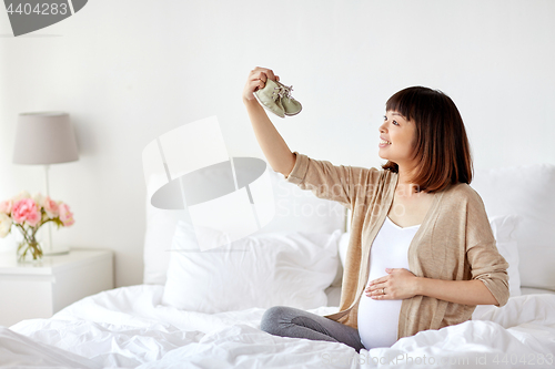 Image of happy pregnant woman with bootees in bed at home