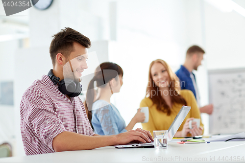 Image of creative man with headphones and laptop at office