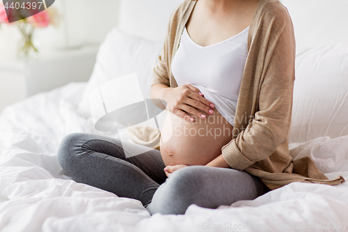 Image of pregnant woman with bare belly sitting in bed