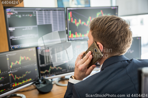 Image of Over the shoulder view of stock broker trading online, talking on mobile phone.