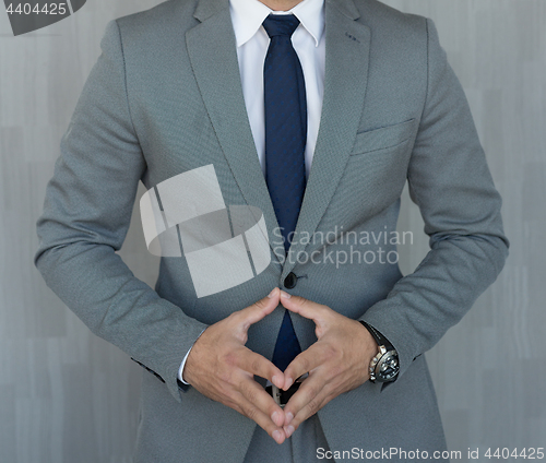 Image of Torso of anonymous businessman standing with hands in lowered steeple wearing beautiful fashionable classic grey suit, white shirt and blue tie.