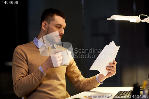 Image of man with papers and coffee working at night office