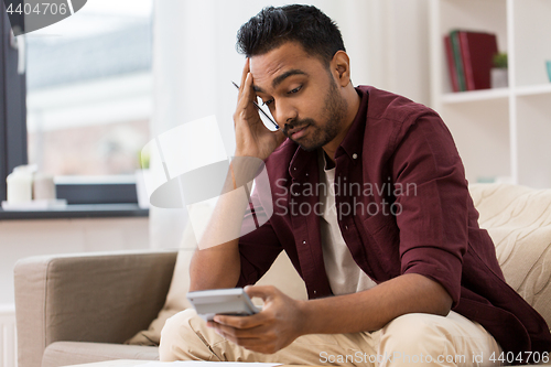 Image of confused man with calculator at home