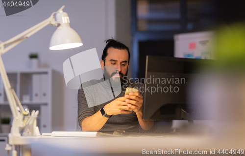 Image of creative man with smartphone at night office