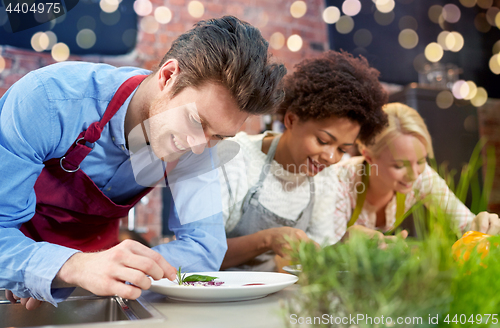 Image of happy friends cooking and decorating dishes