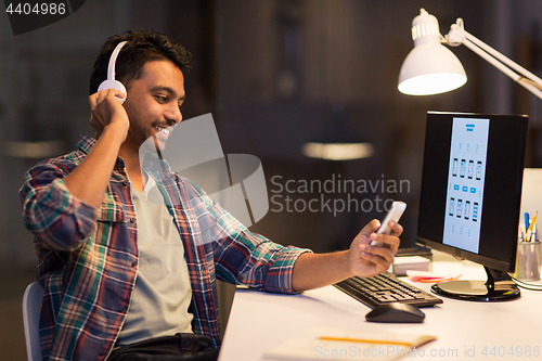Image of man with headphones and smartphone at night office