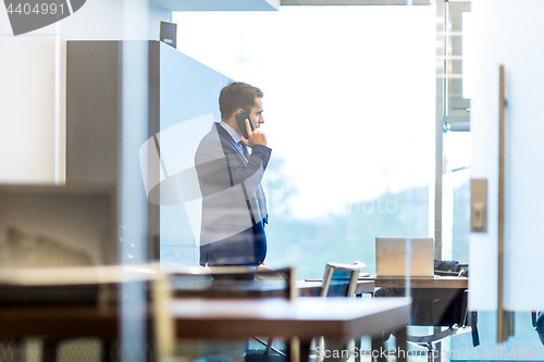 Image of Businessman talking on a mobile phone while looking through window.