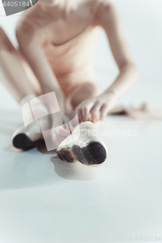 Image of Beautiful little ballerina in blue dress for dancing puting on foot pointe shoes