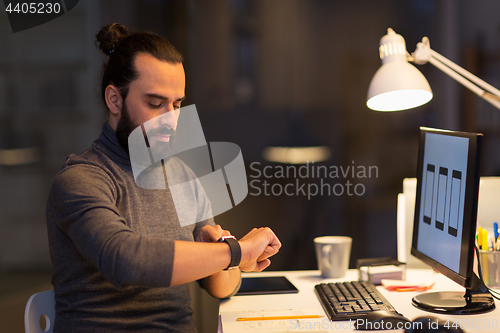 Image of man with smartwatch and computer at night office