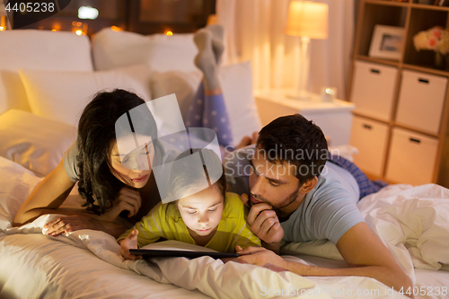 Image of family with tablet pc in bed at night at home