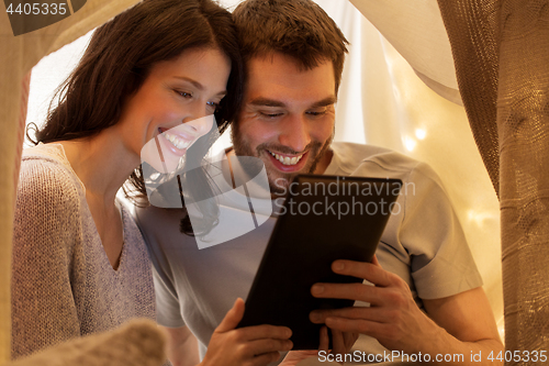 Image of happy couple with tablet pc in kids tent at home