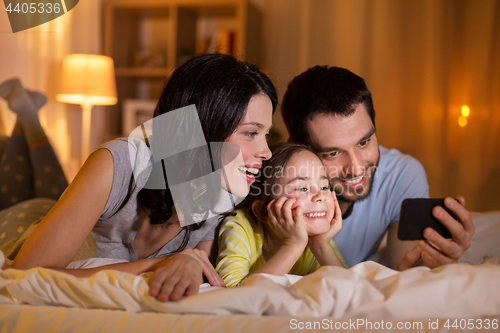 Image of happy family with smartphone in bed at night