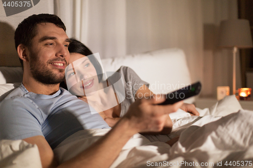 Image of happy couple watching tv in bed at night at home