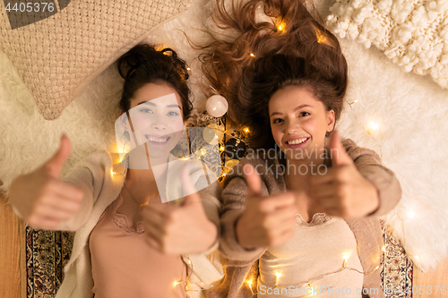 Image of happy female friends showing thumbs up at home