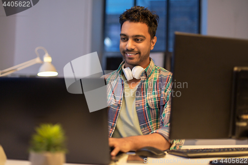 Image of creative man with laptop working at night office