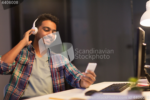 Image of man with headphones and smartphone at night office