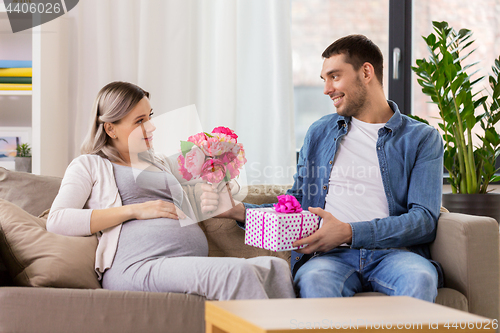 Image of man giving flowers to pregnant woman at home