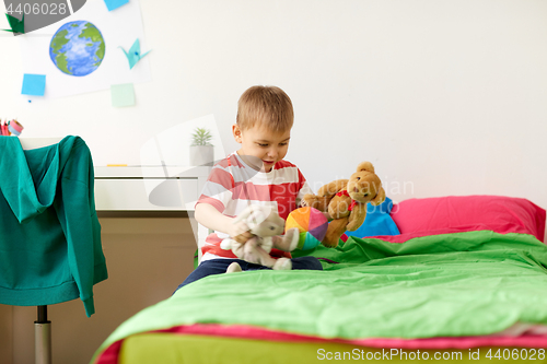 Image of happy little boy playing with plush toys at home