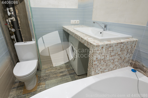 Image of Unfinished repairs in the bathroom, a pedestal under the washbasin, under which there is a washing machine, and a toilet bowl
