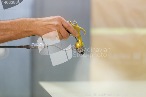 Image of worker hand sprays urethane finish to board