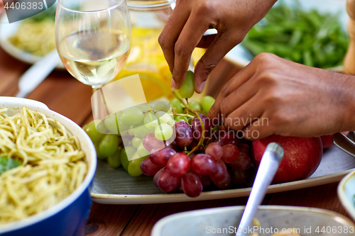 Image of hands taking grape from plate with fruits