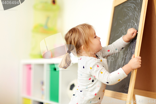 Image of happy little girl drawing on chalk board at home