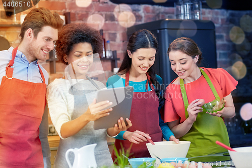 Image of happy friends with tablet pc cooking in kitchen