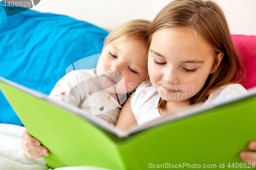 Image of little girls or sisters reading book in bed