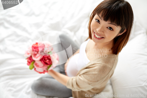 Image of happy asian pregnant woman with flowers in bed