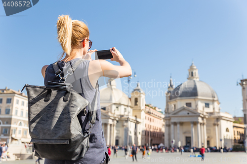 Image of Female tourist with a fashinable vintage hipster backpack taking photo of Piazza del Popolo in Rome, Italy by her mobile phone.