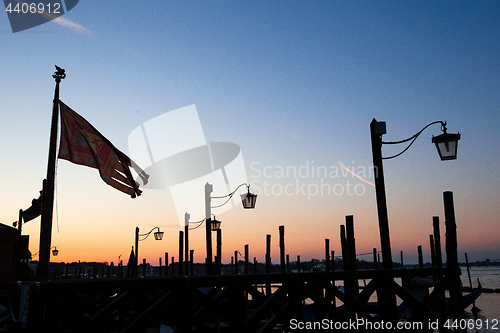Image of Venice, Italy - street lamps and city flag silhouettes at sunris