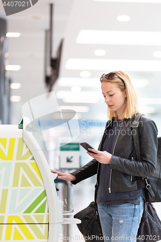 Image of Casual caucasian woman using smart phone application and check-in machine at the airport getting the boarding pass.