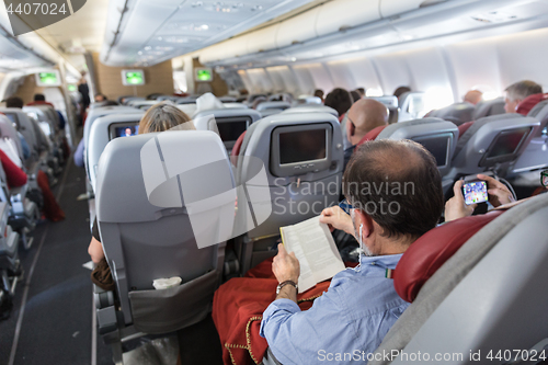 Image of Interior of large commercial airplane with passengers on their seats during flight.