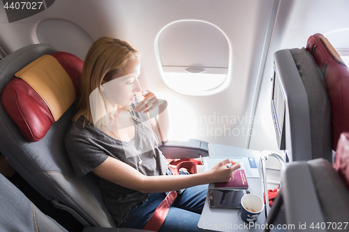 Image of Woman filling immigration form on commercial passengers airplane during flight.