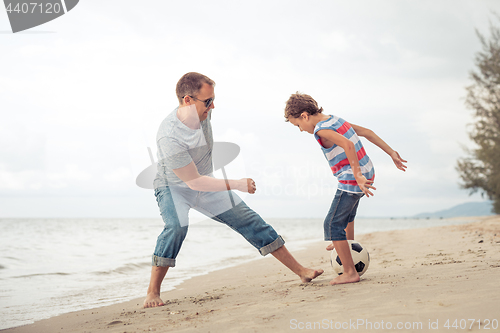 Image of Father and son playing football on the beach at the day time.