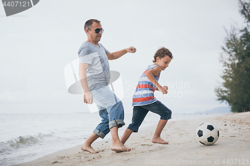 Image of Father and son playing football on the beach at the day time.