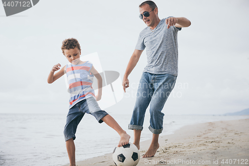 Image of Father and son playing football on the beach at the day time. 