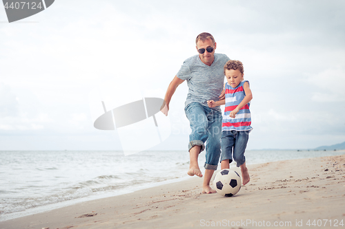 Image of Father and son playing football on the beach at the day time.