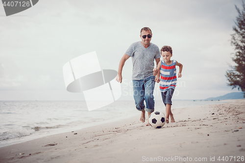 Image of Father and son playing football on the beach at the day time.