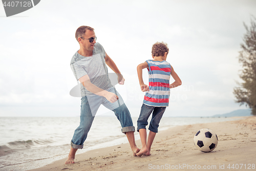 Image of Father and son playing football on the beach at the day time.