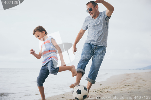 Image of Father and son playing football on the beach at the day time.