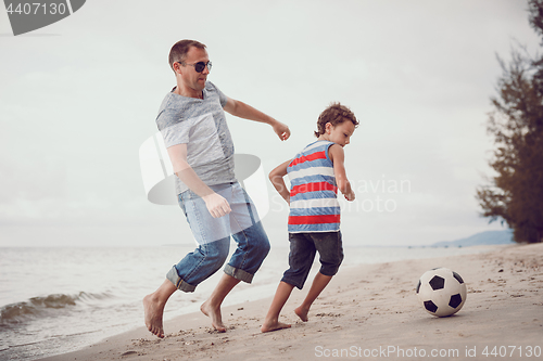 Image of Father and son playing football on the beach at the day time.